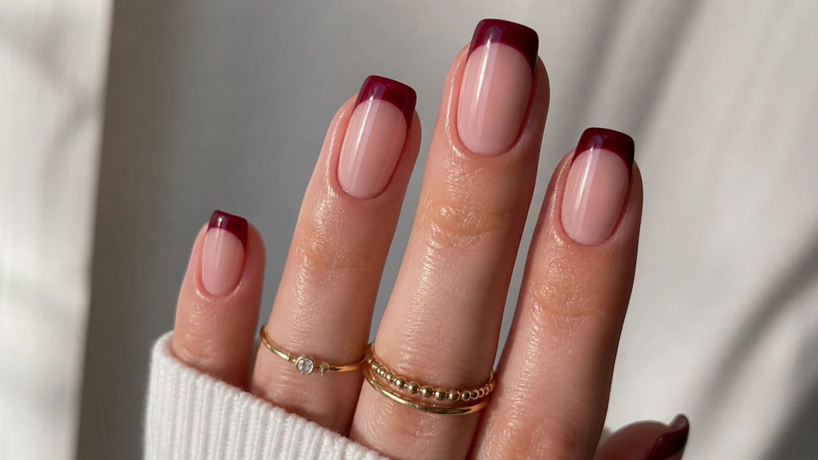 Squoval nails with a sheer nude base and deep wine French tips