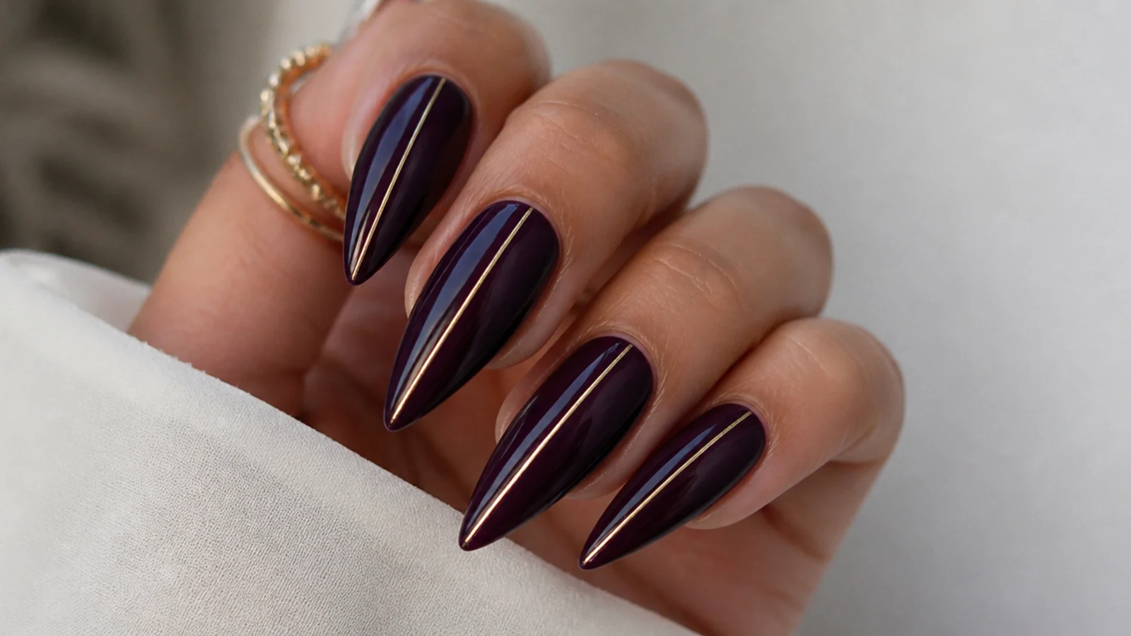 Stiletto nails in deep blackcurrant purple with a fine gold line down the center