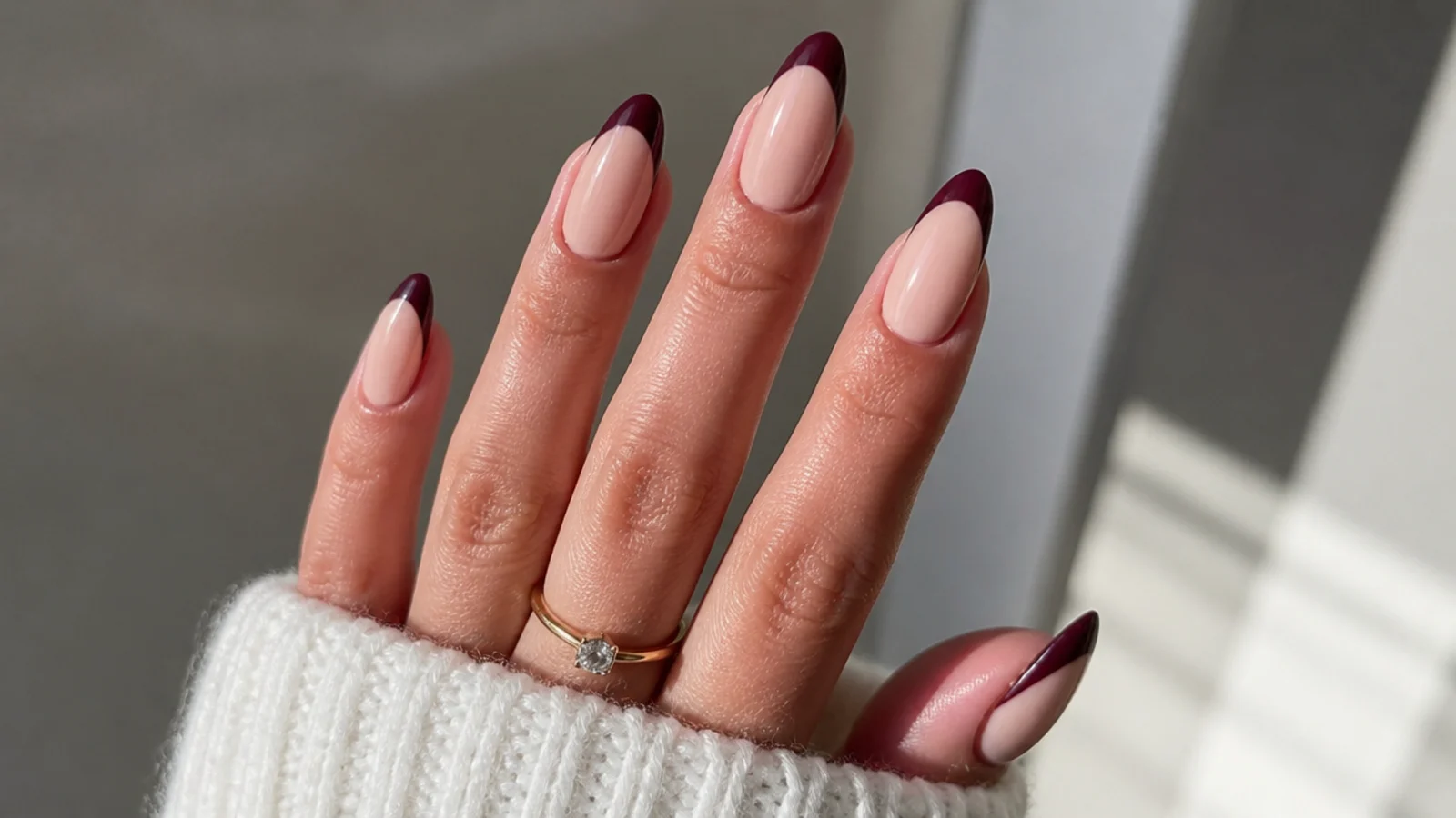 Nude nails with deep burgundy French tips on an almond shape