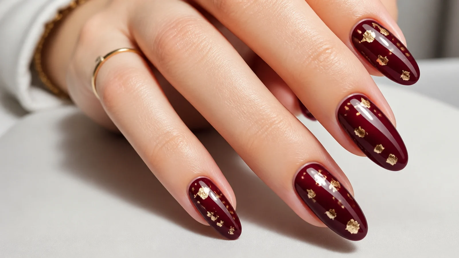 Deep oxblood nails scattered with fine gold leaf flakes