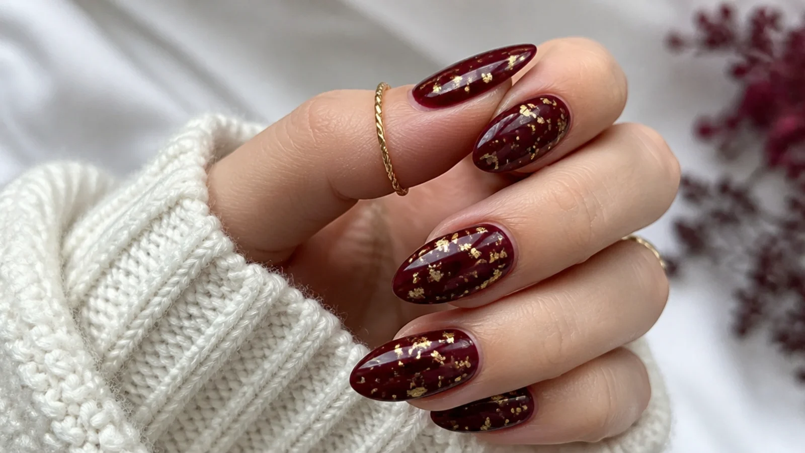 Deep oxblood almond nails with fine gold foil flecks scattered across the surface