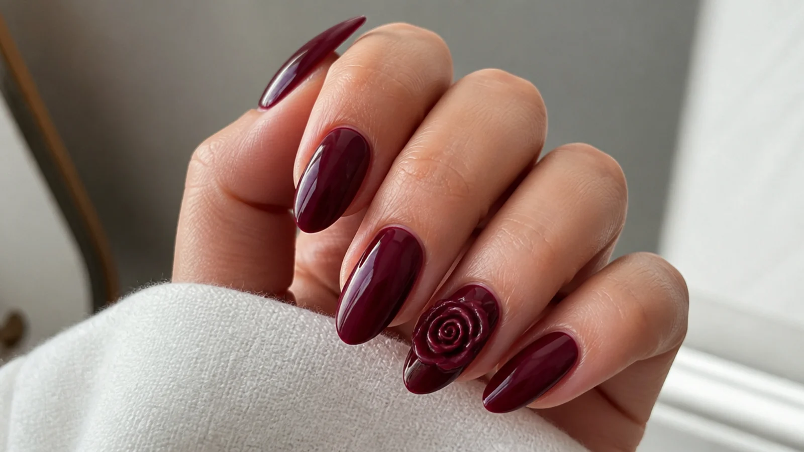 Deep wine almond nails with a single sculpted 3D rose on the ring finger