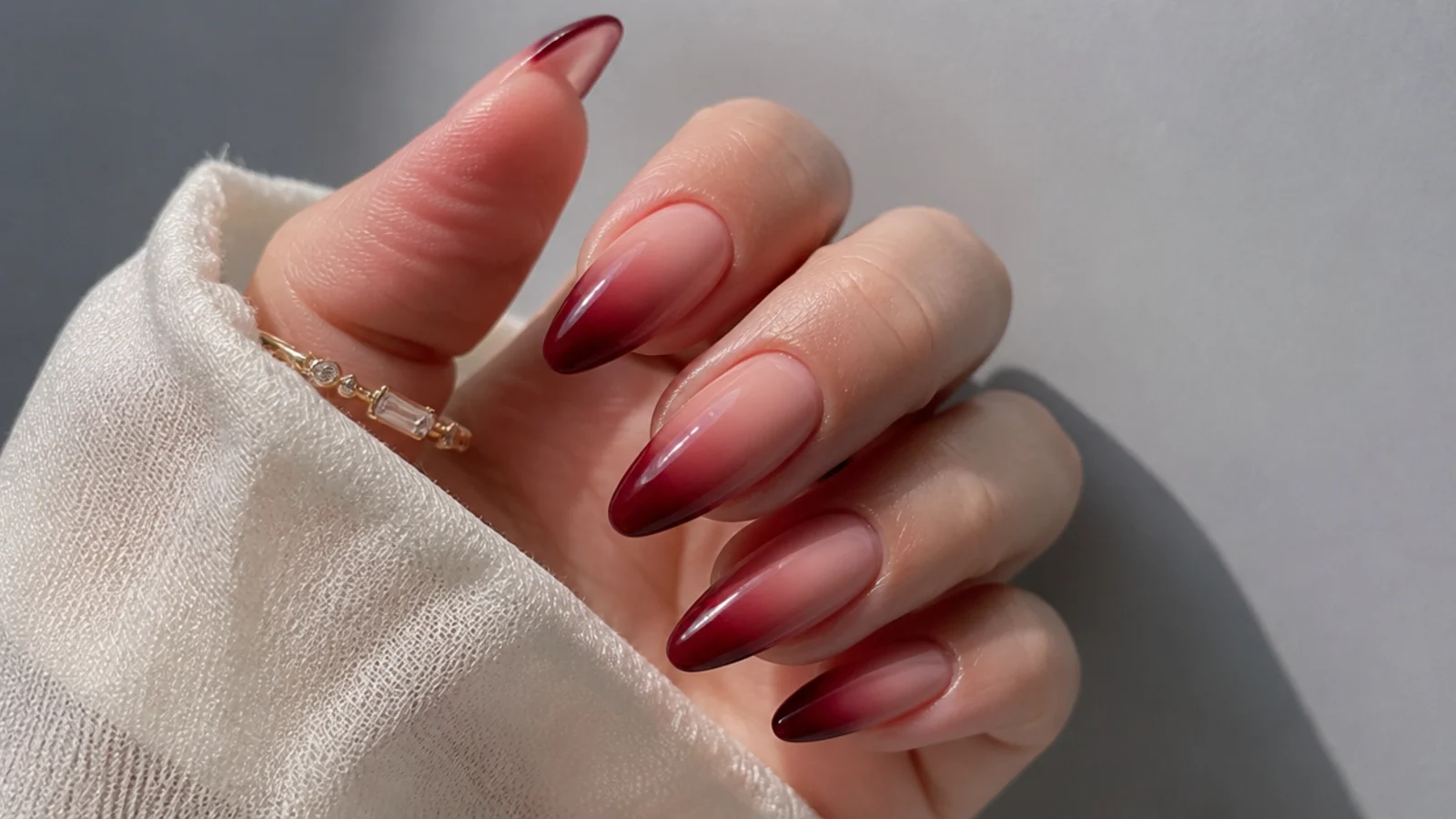 Warm sheer-to-deep red almond nails fading darker toward the tips