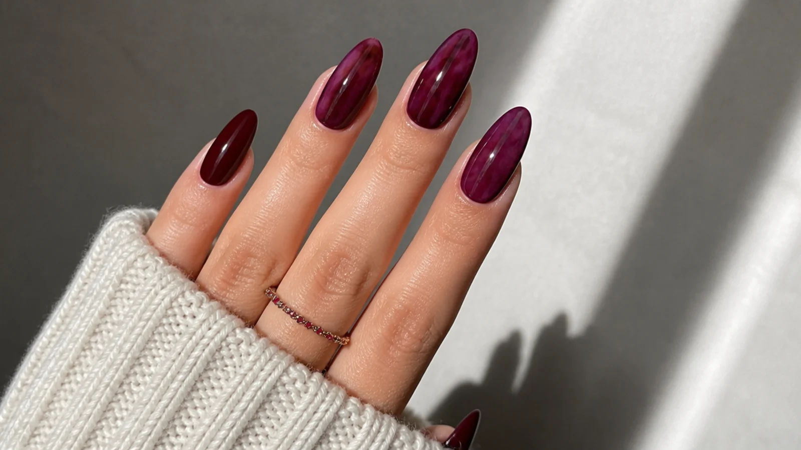 Glossy oxblood and berry dark feminine nails on an almond shape against soft light