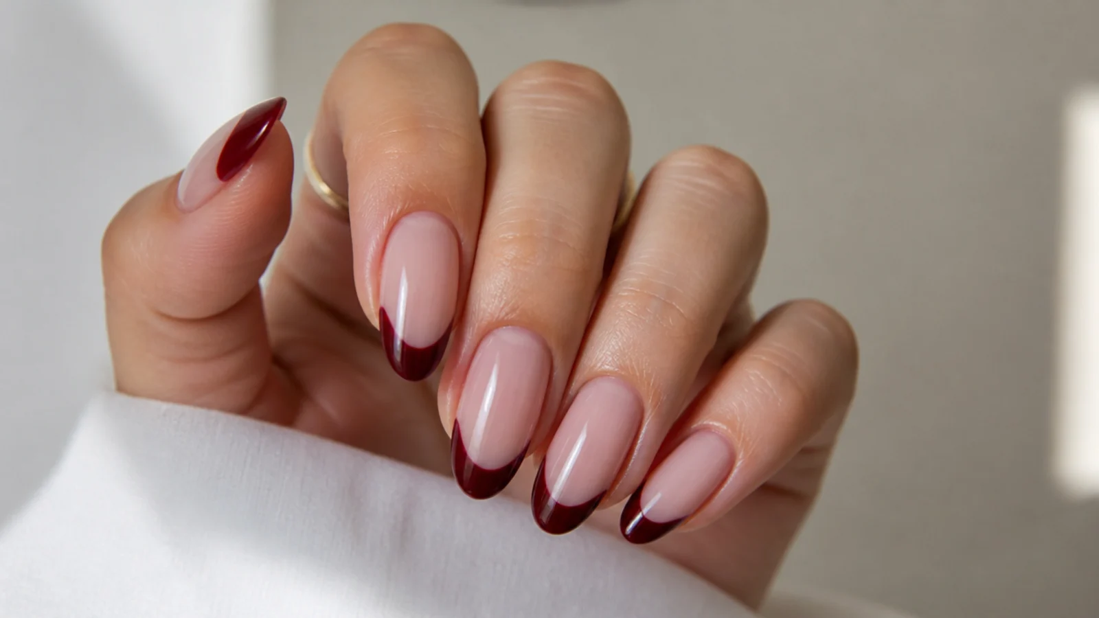 Sheer nude nails with deep burgundy French tips on almond shape