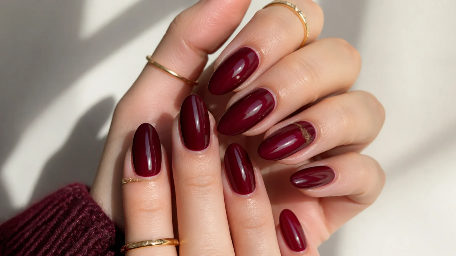 Deep oxblood red almond nails with a glossy finish on styled hands