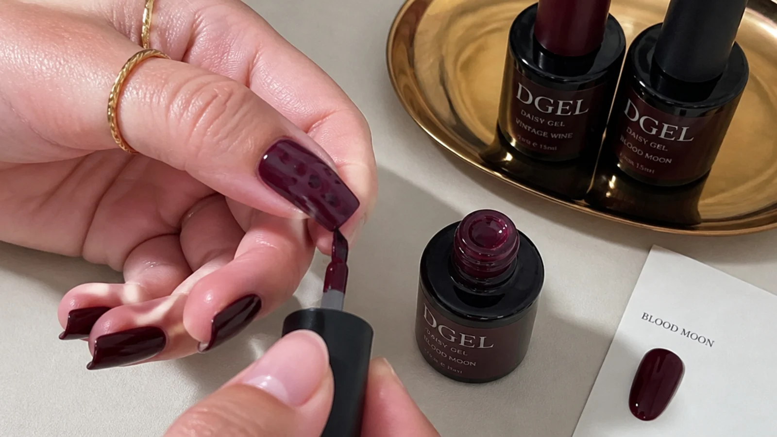 Dark feminine gel supplies with a berry square nail mid-application