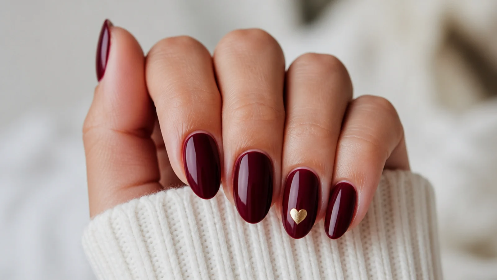 Oxblood nails with a small gold foil heart accent on the ring finger