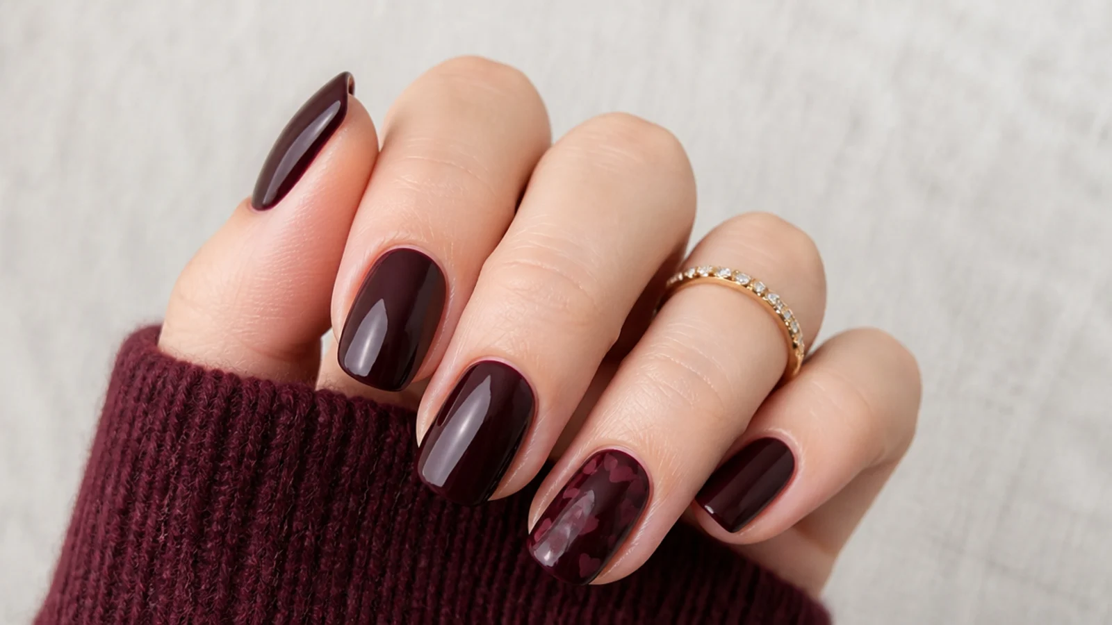 Deep black cherry nails with tiny tonal hearts scattered on one nail