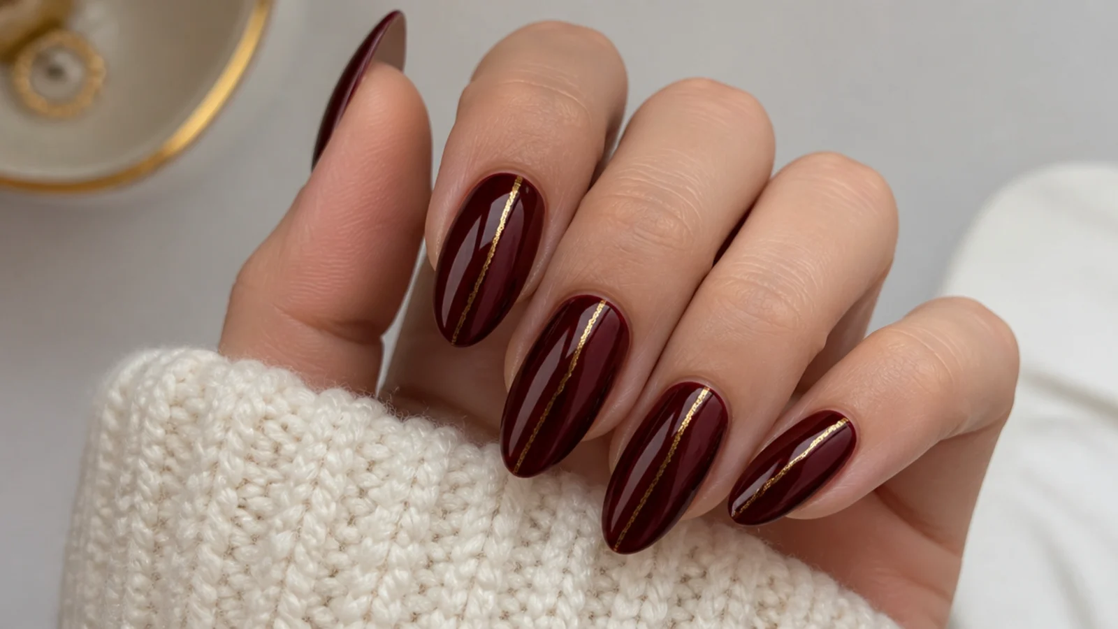 Oxblood almond nails with a thin gold foil accent line