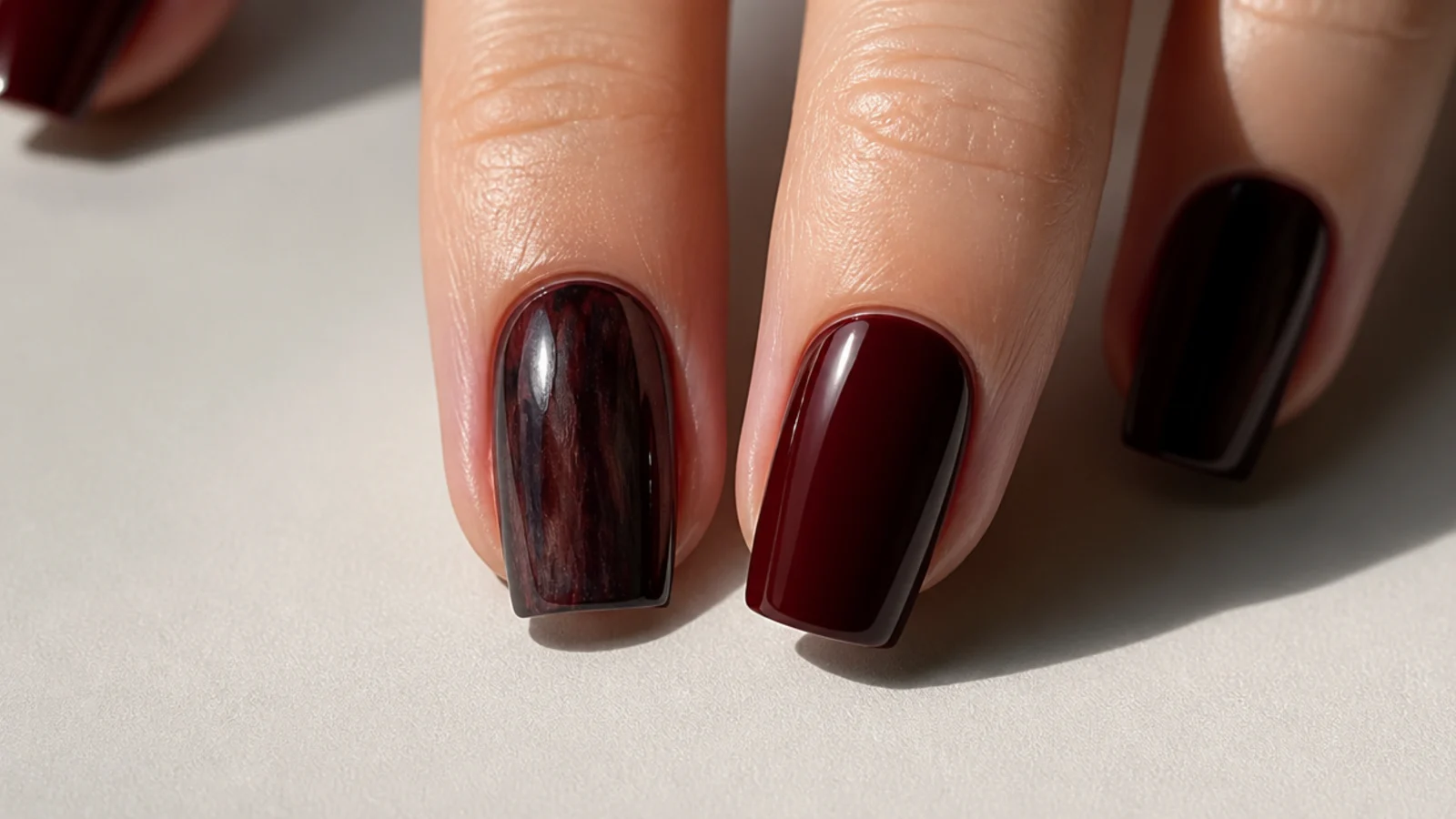 A streaky patchy dark nail next to a smooth glossy oxblood one for comparison