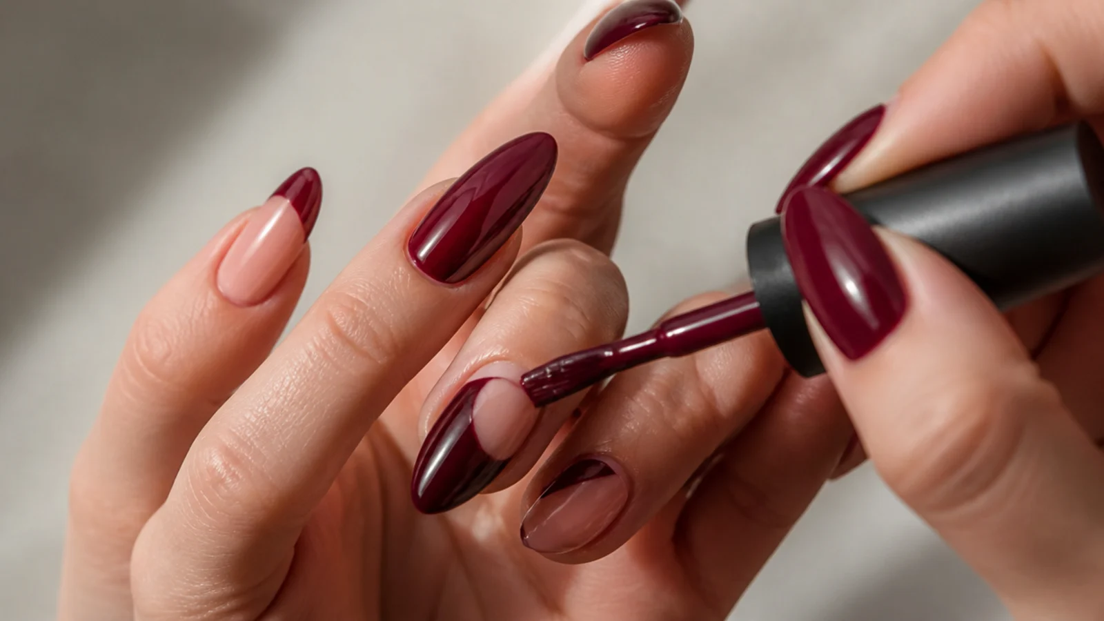 A deep berry gel color being layered onto an almond nail, hands only