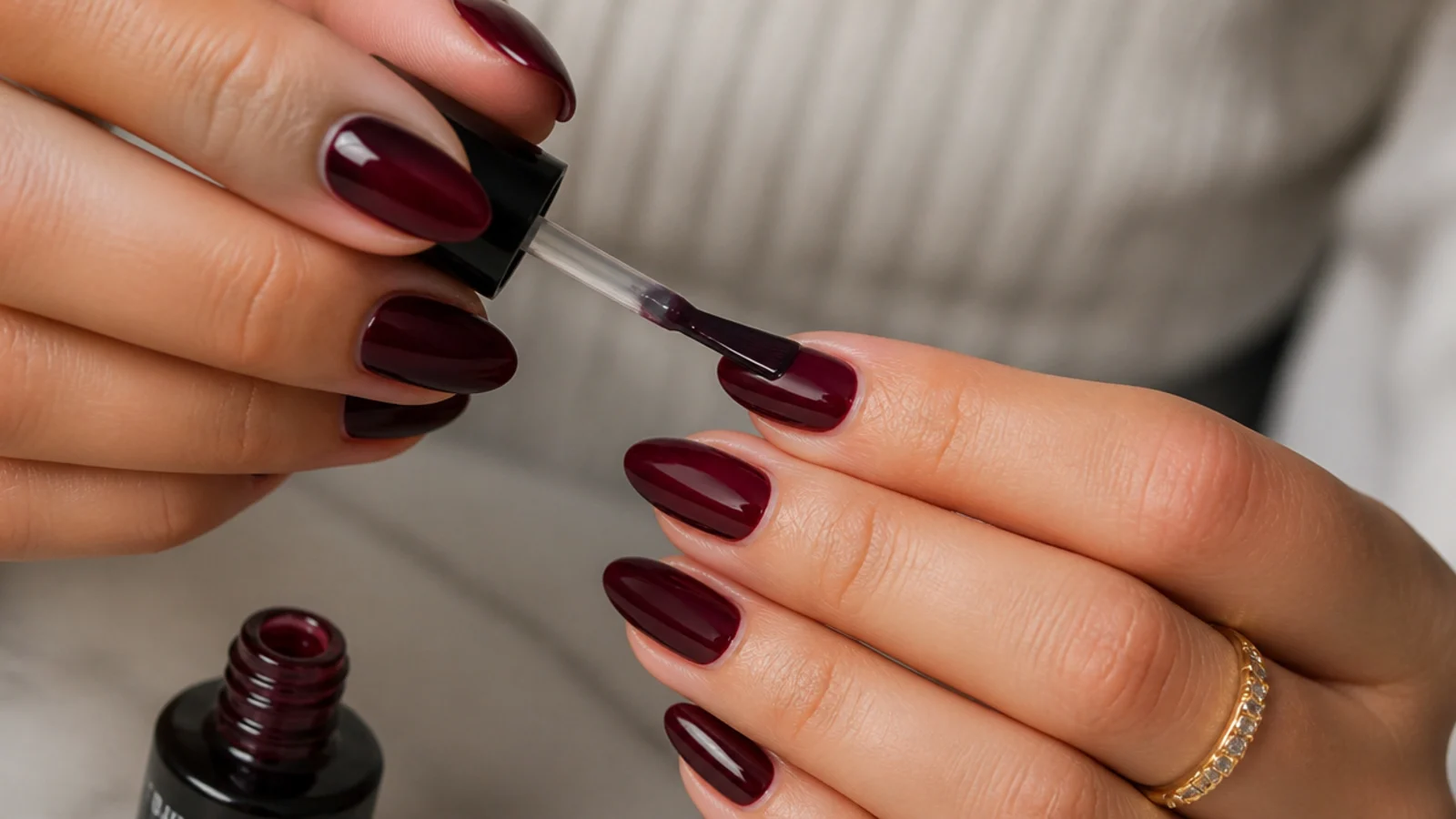 A glossy top coat sealing deep oxblood almond nails, hands only