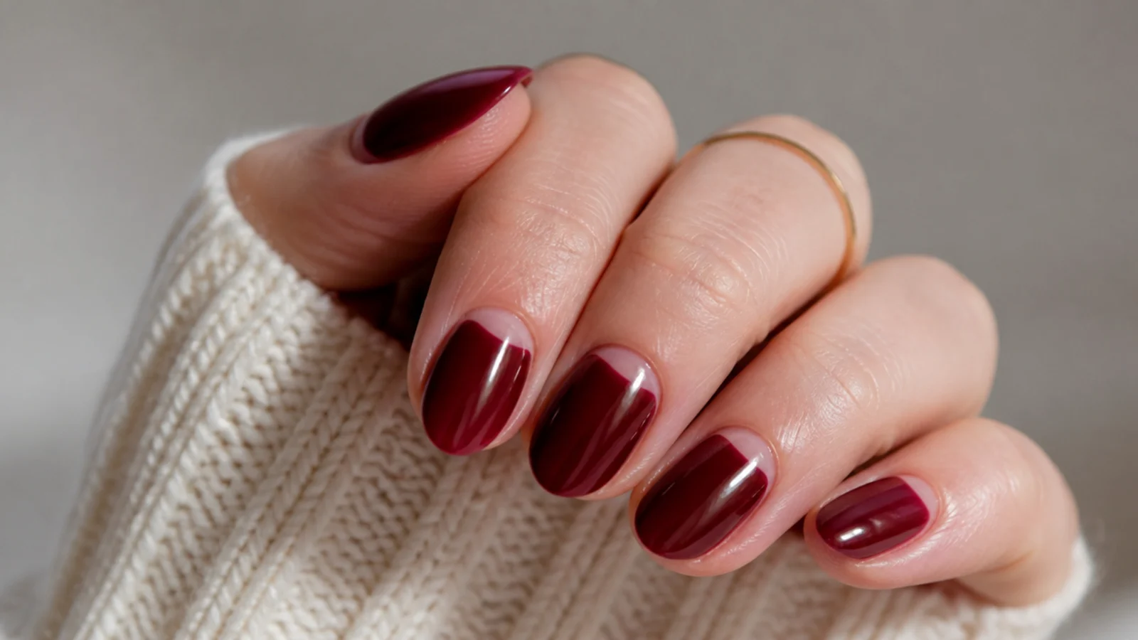 Short almond nails in oxblood with a bare negative-space half-moon at the cuticle