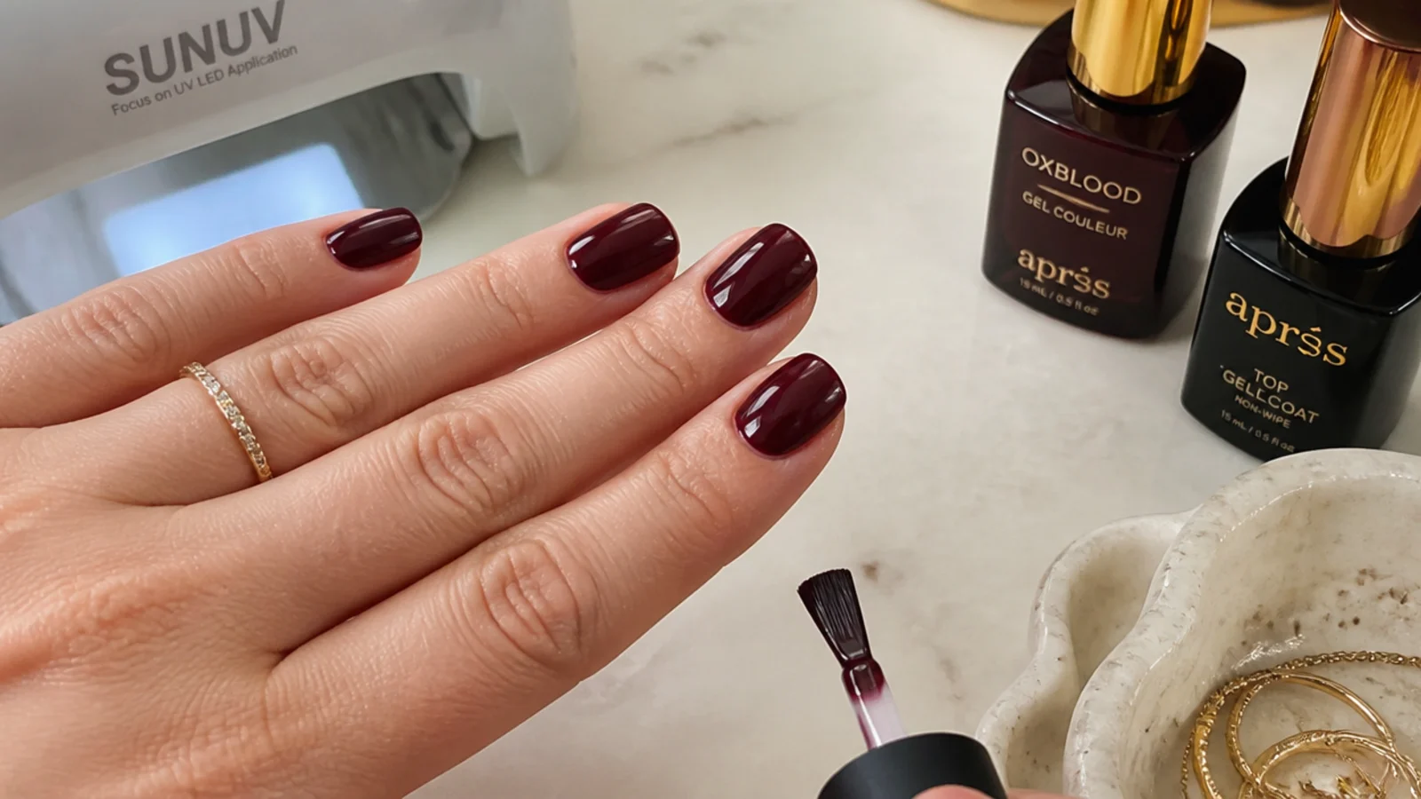 Short nails mid-application with deep oxblood gel, lamp and top coat