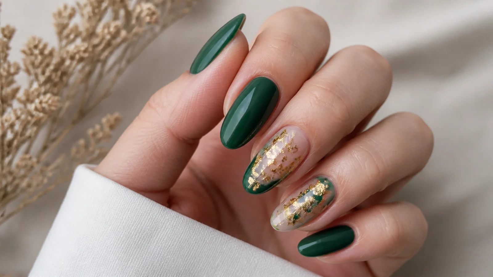 Emerald green acrylic nails with gold foil accents on an almond shape
