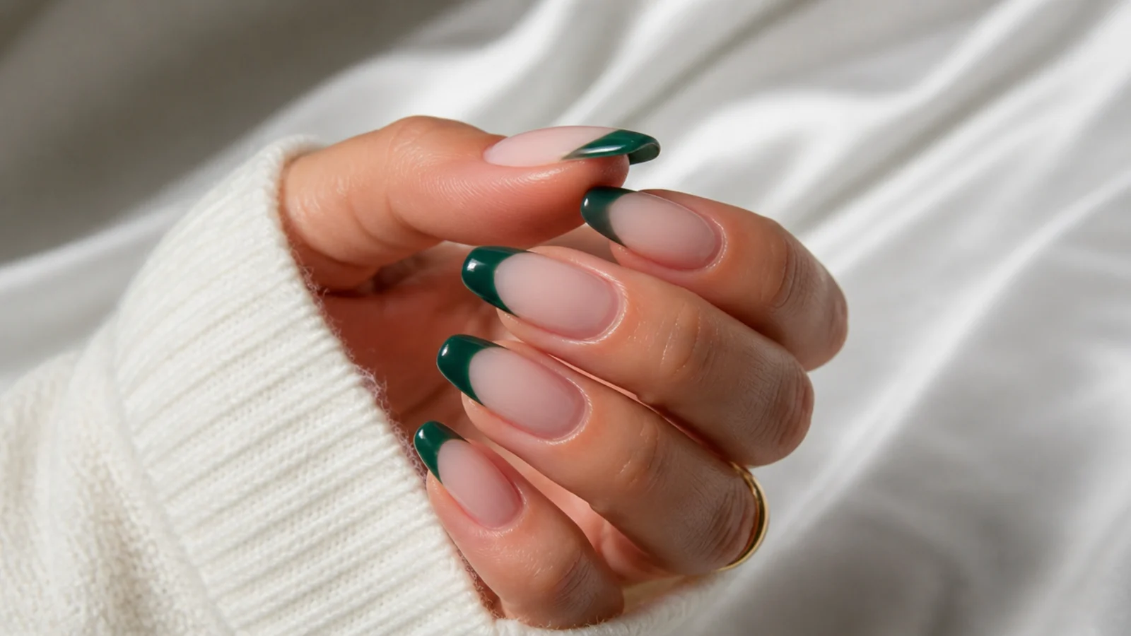 Nude acrylic nails with emerald green french tips on an almond shape