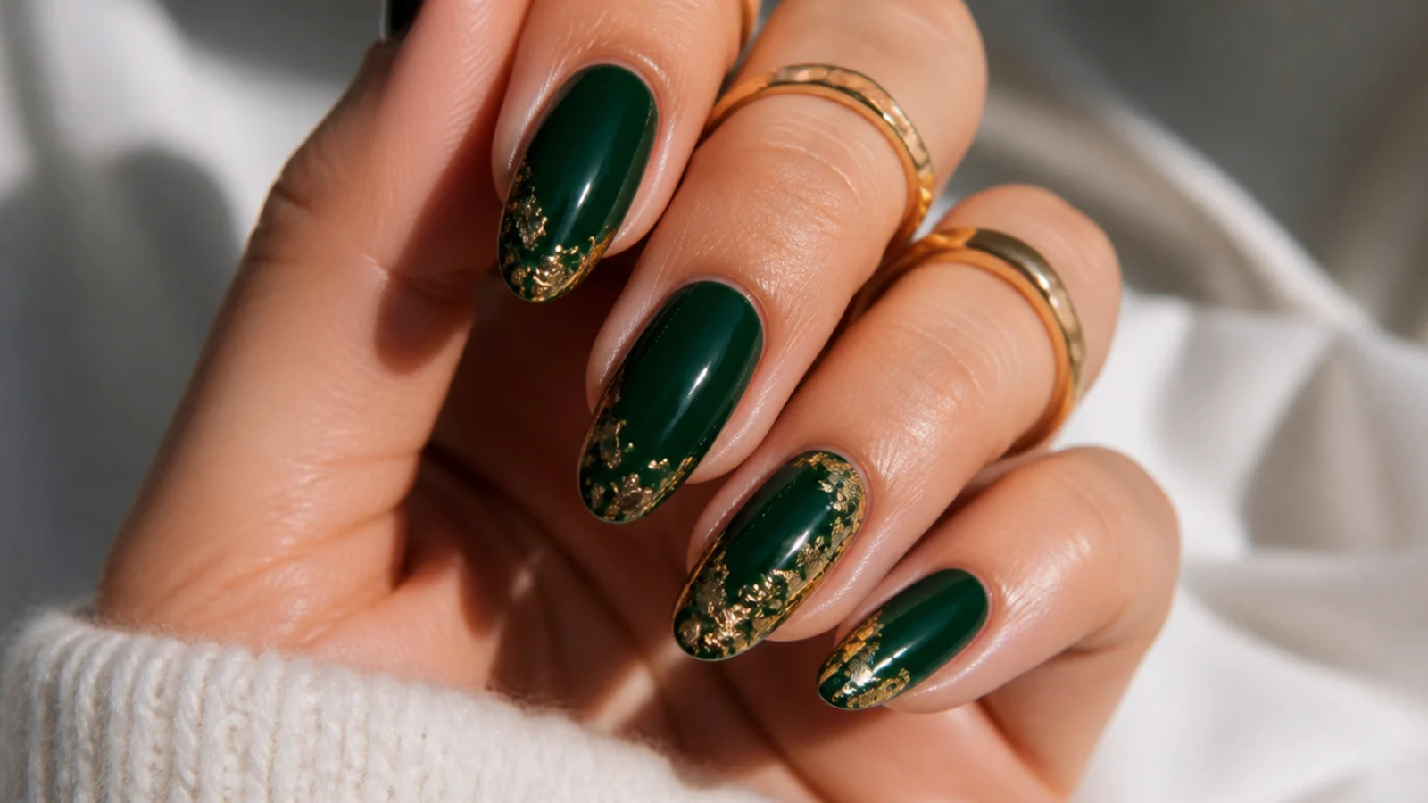 Deep emerald green nails with gold foil accents on almond shapes