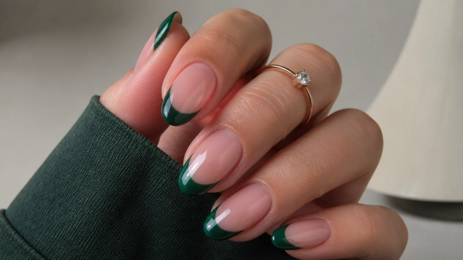 Glossy emerald green french tip nails on an almond shape over a nude base