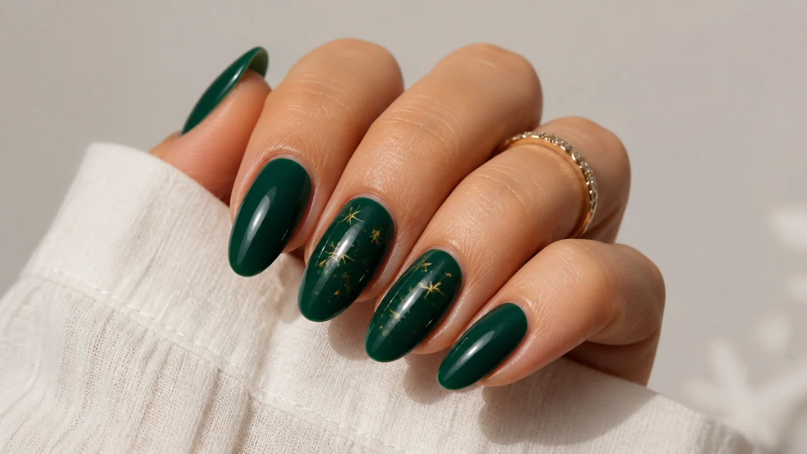 Deep emerald green glossy nails on an almond shape against a neutral background