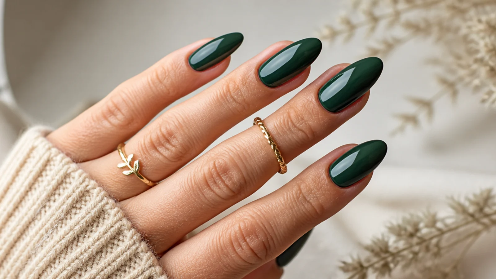 Deep emerald green glossy nails on an almond shape against a neutral background