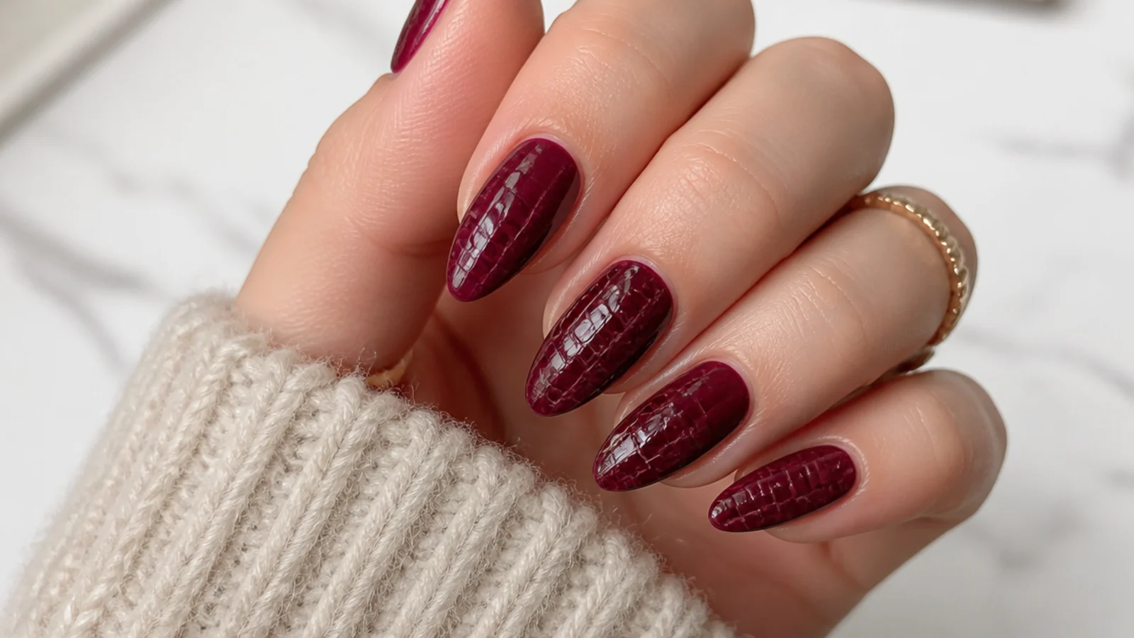 Deep burgundy almond December nails with a tonal croc-print texture