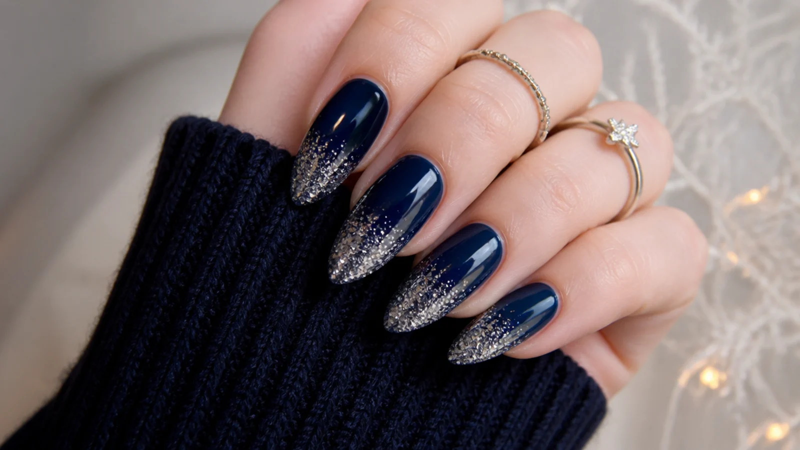 Deep navy almond December nails with a silver glitter gradient at the tips