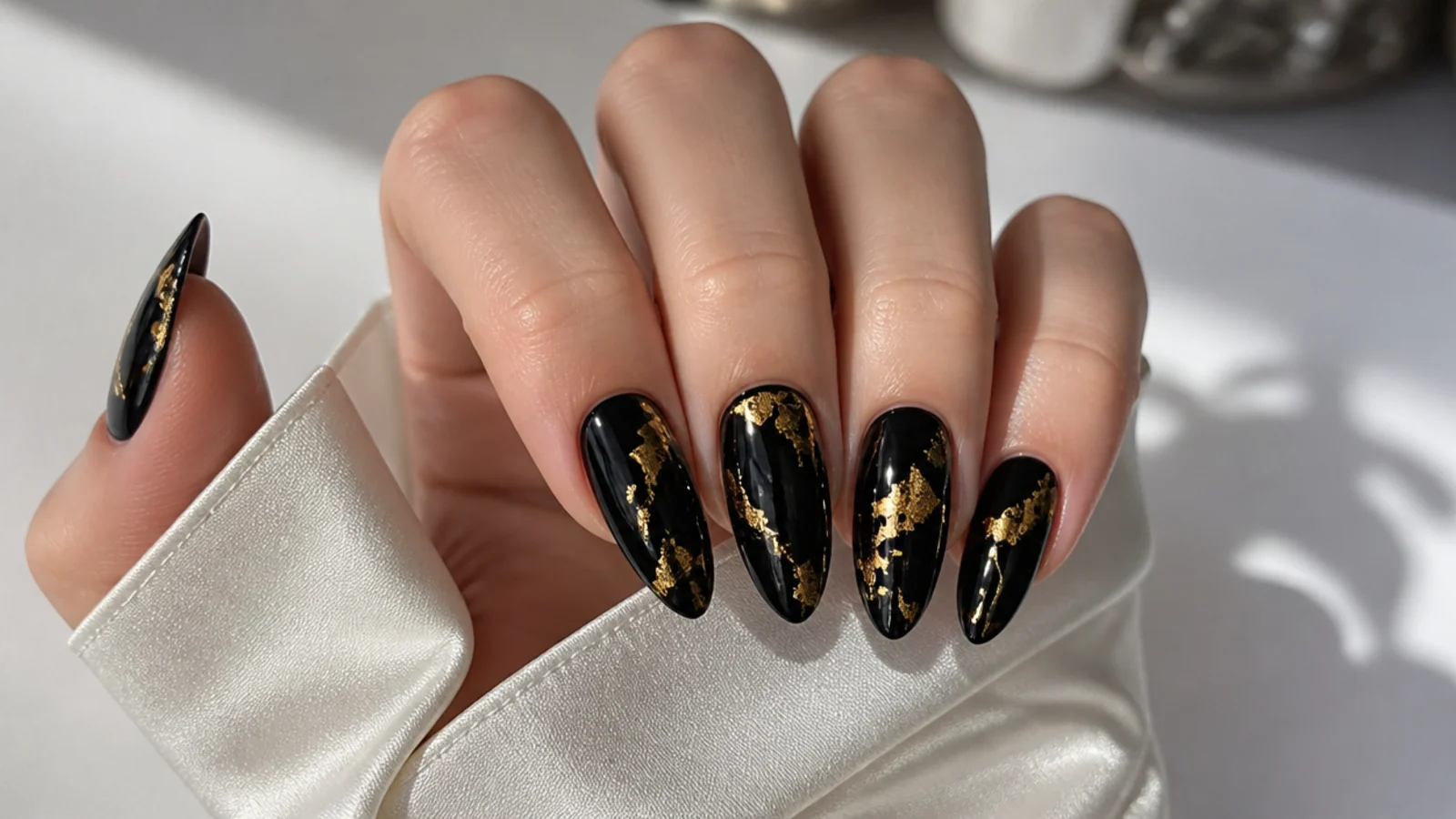 Glossy black almond December nails with cracked gold foil accents