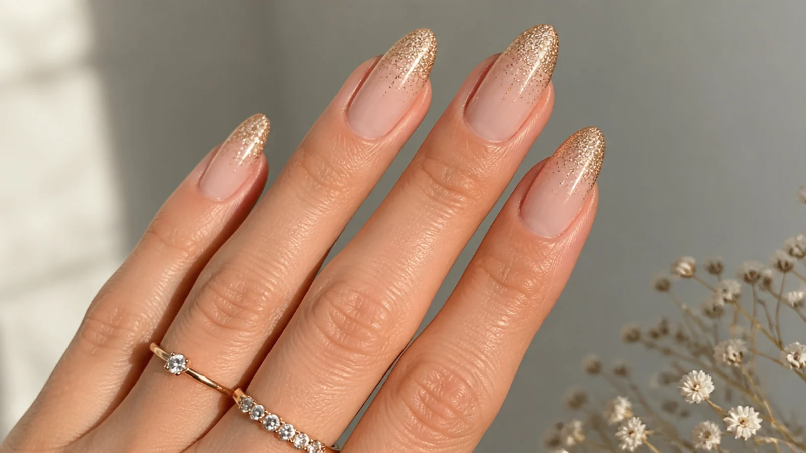 Almond nails with a nude base fading into champagne gold glitter at the tips