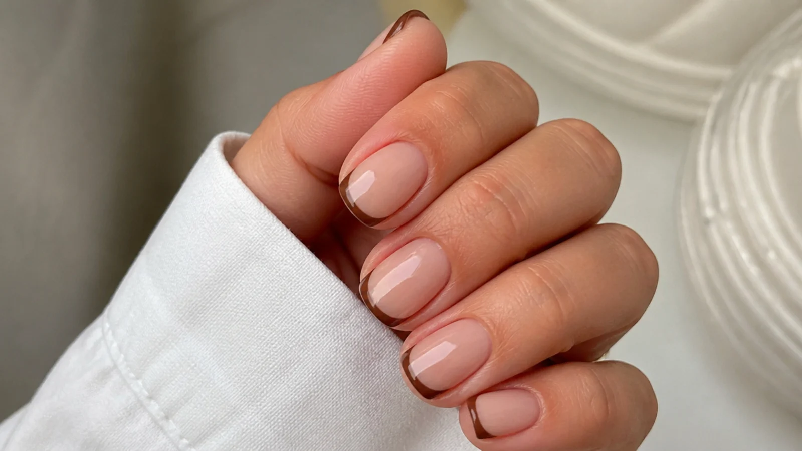 Short round nails with a nude base and thin chocolate brown French tips
