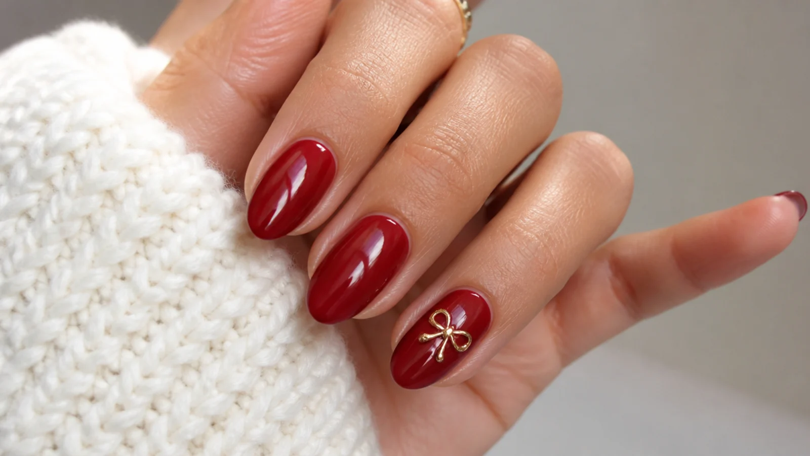 Short almond nails in glossy red with a tiny gold micro-bow charm on one nail