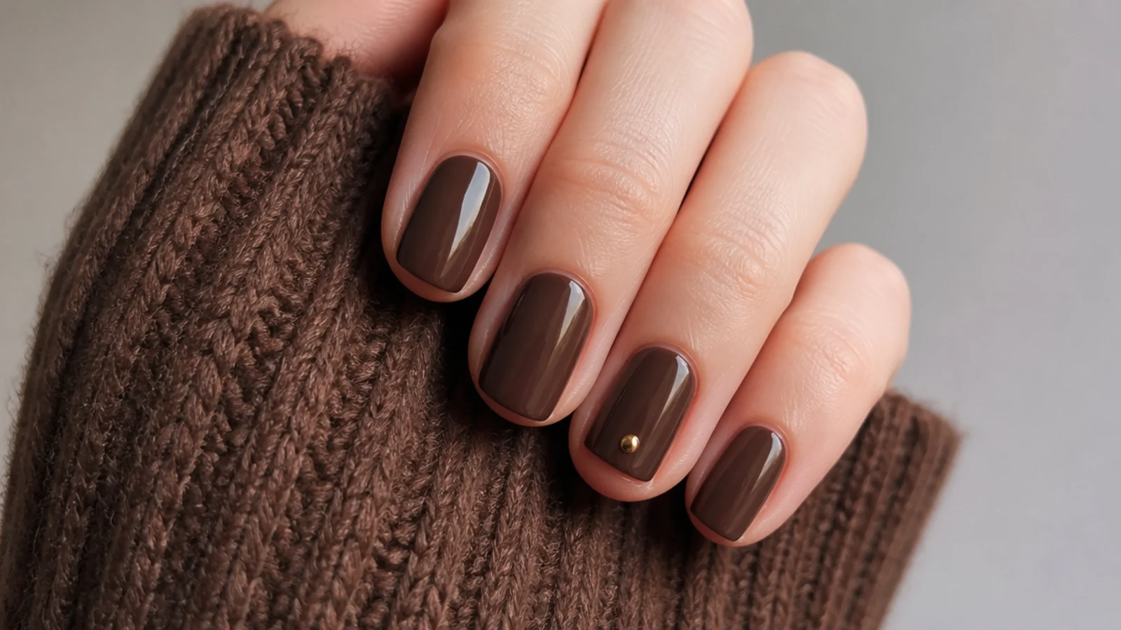 Short cozy brown December nails with a single tiny gold dot accent