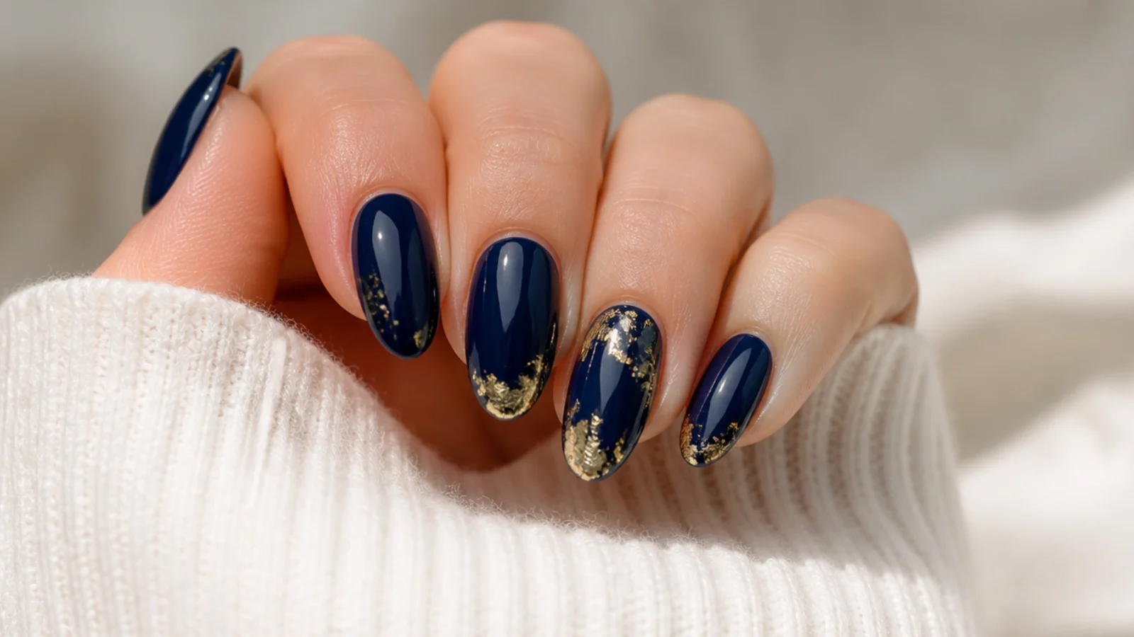 Deep navy December nails with gold foil flakes on almond tips