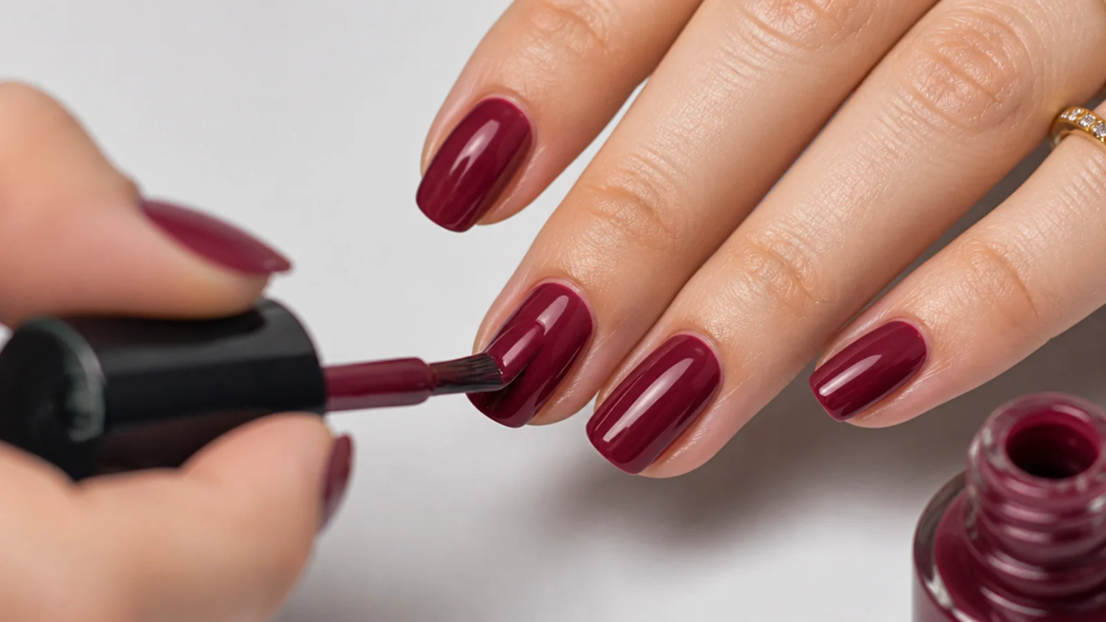 Two thin coats of deep cranberry gel being painted over the whole nail