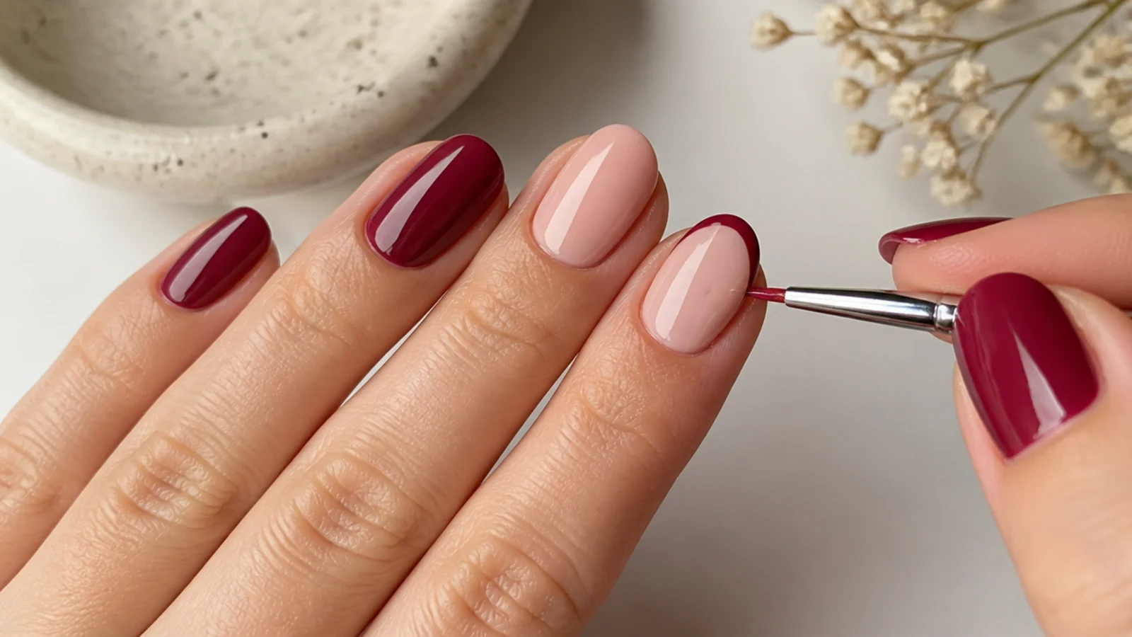 A thin liner brush painting a cranberry micro-French tip on an accent nail