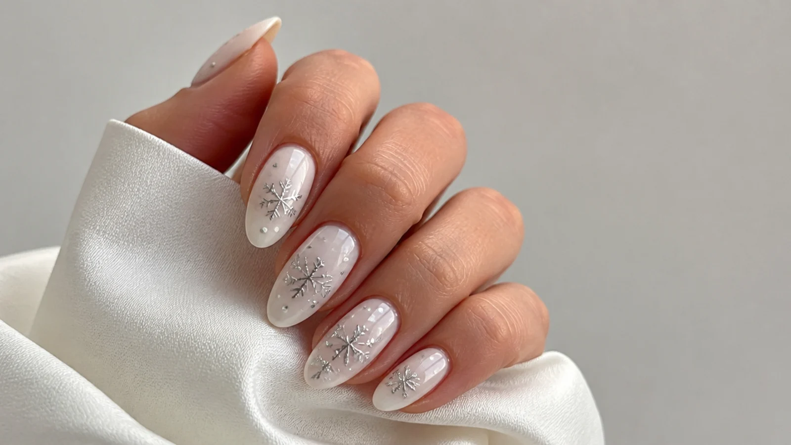 Milky white December nails with tiny silver snowflake accents on an almond shape
