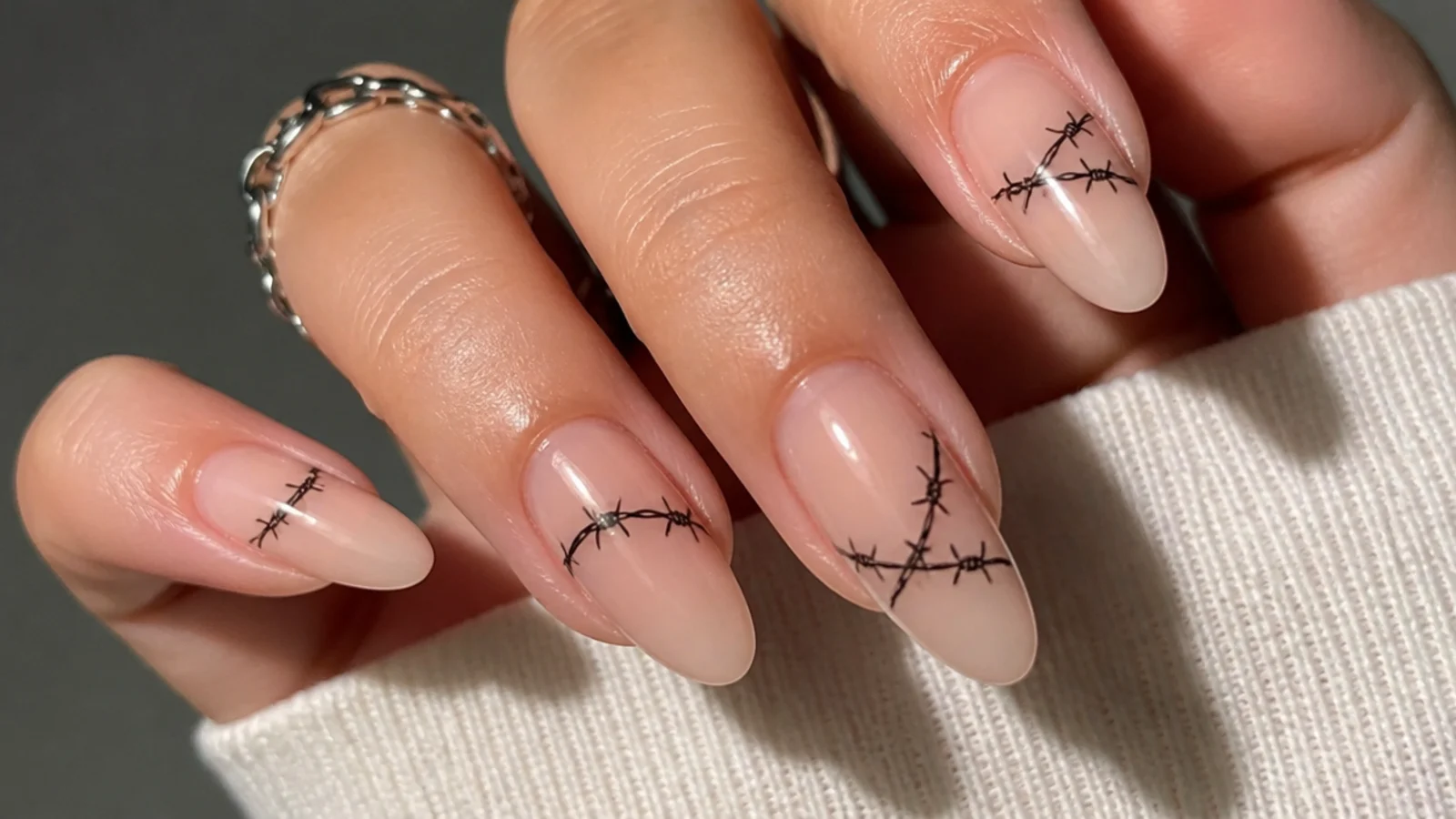 Nude emo nails with fine black barbed-wire line art wrapping the nail