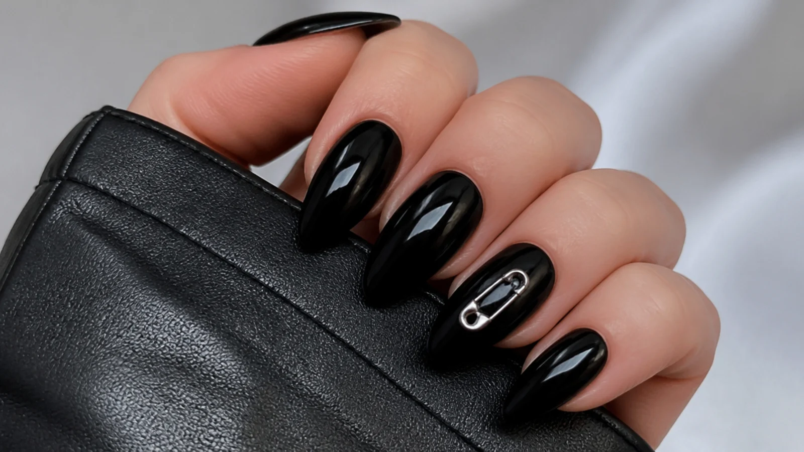 Black emo nails with a small silver safety-pin charm on one accent nail