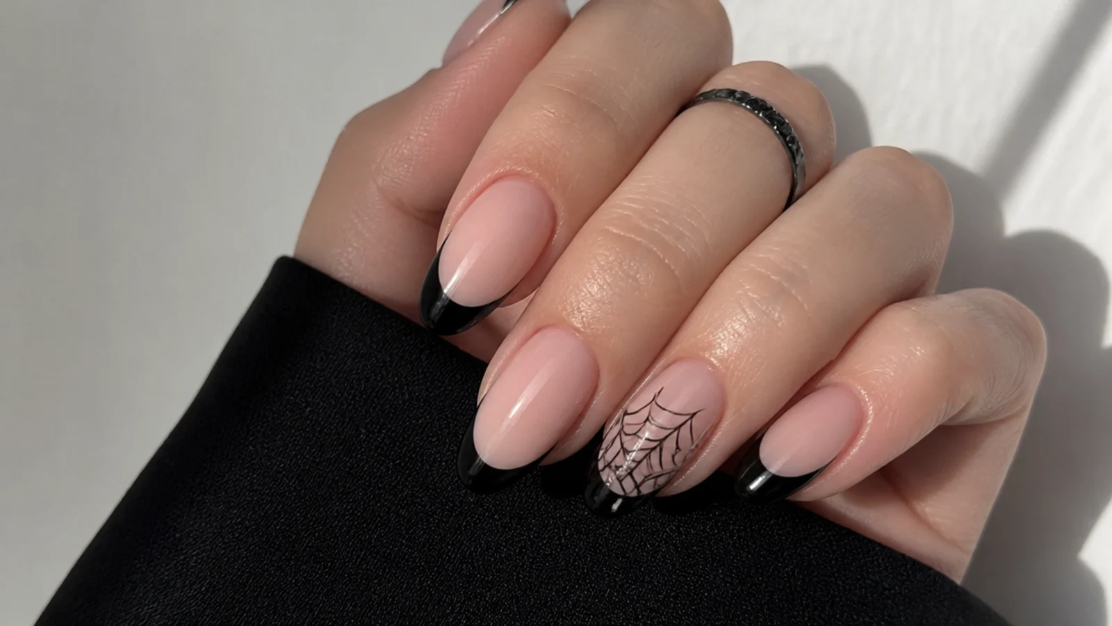 Nude emo nails with black French tips and a fine spiderweb accent