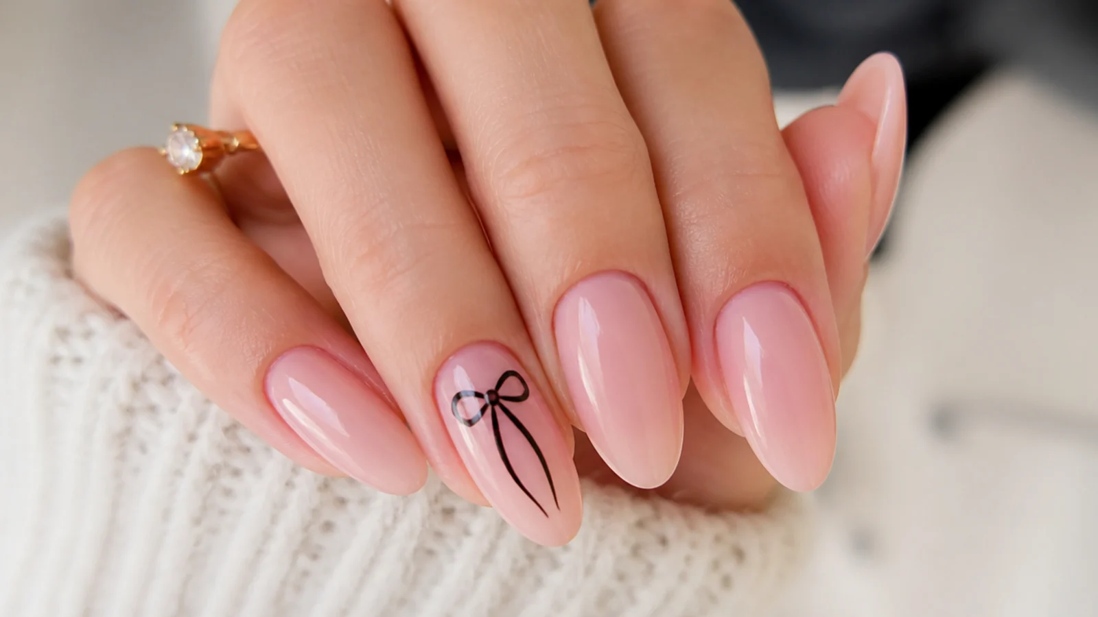 Soft pink nails with a small black hand-painted bow on the accent nail