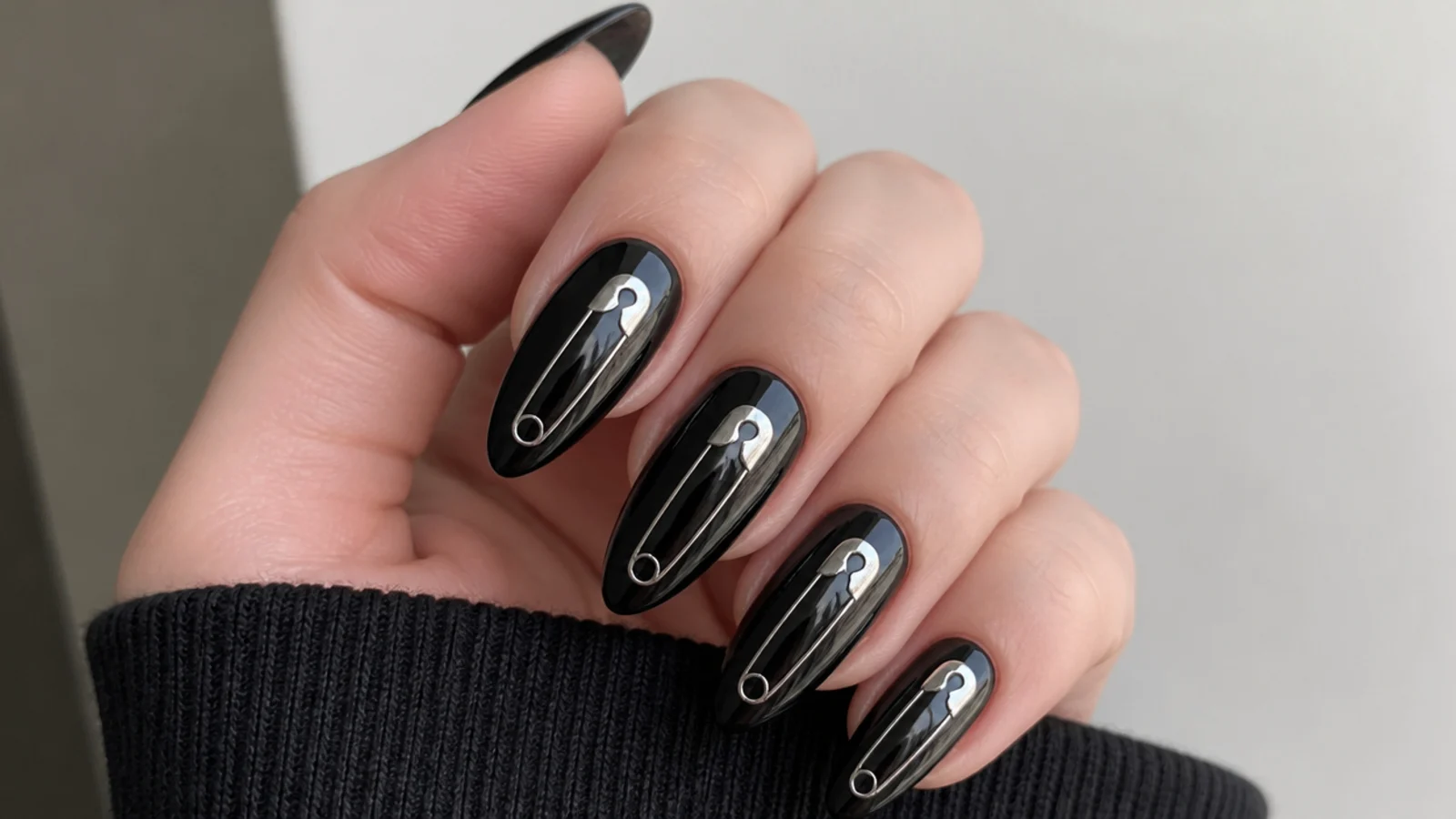 Silver safety pin detail painted across black acrylic nails