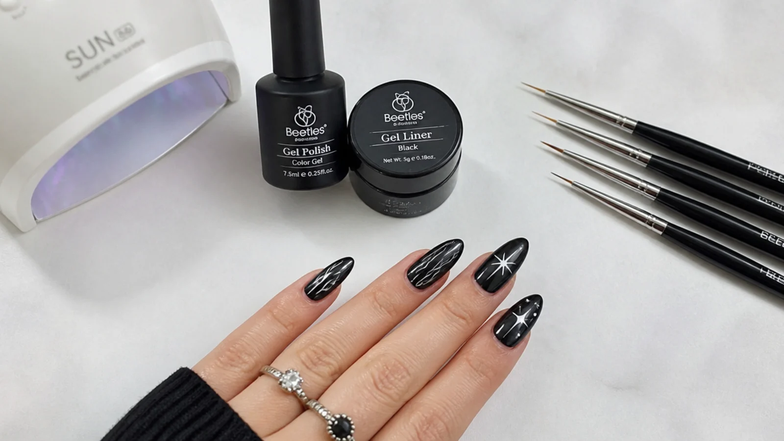 Black gel, liner brushes and a lamp laid out for DIY emo nails