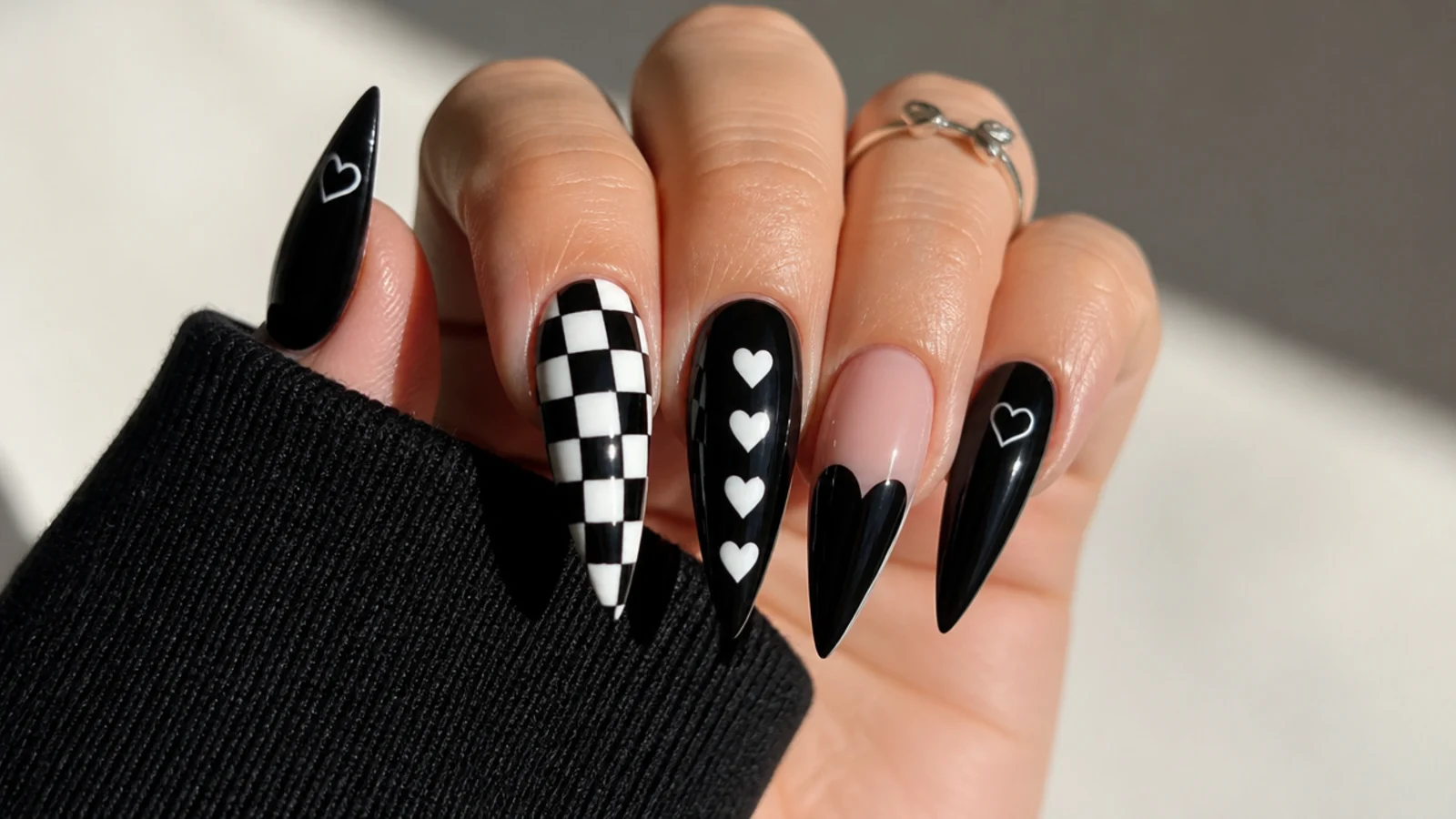 Glossy black emo acrylic nails with checkerboard and heart accents on a stiletto shape