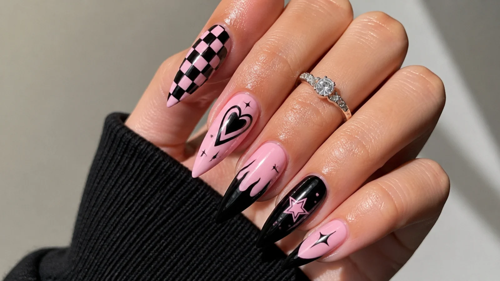 Edgy black and pink emo baddie nails with checkerboard and heart accents on a stiletto shape