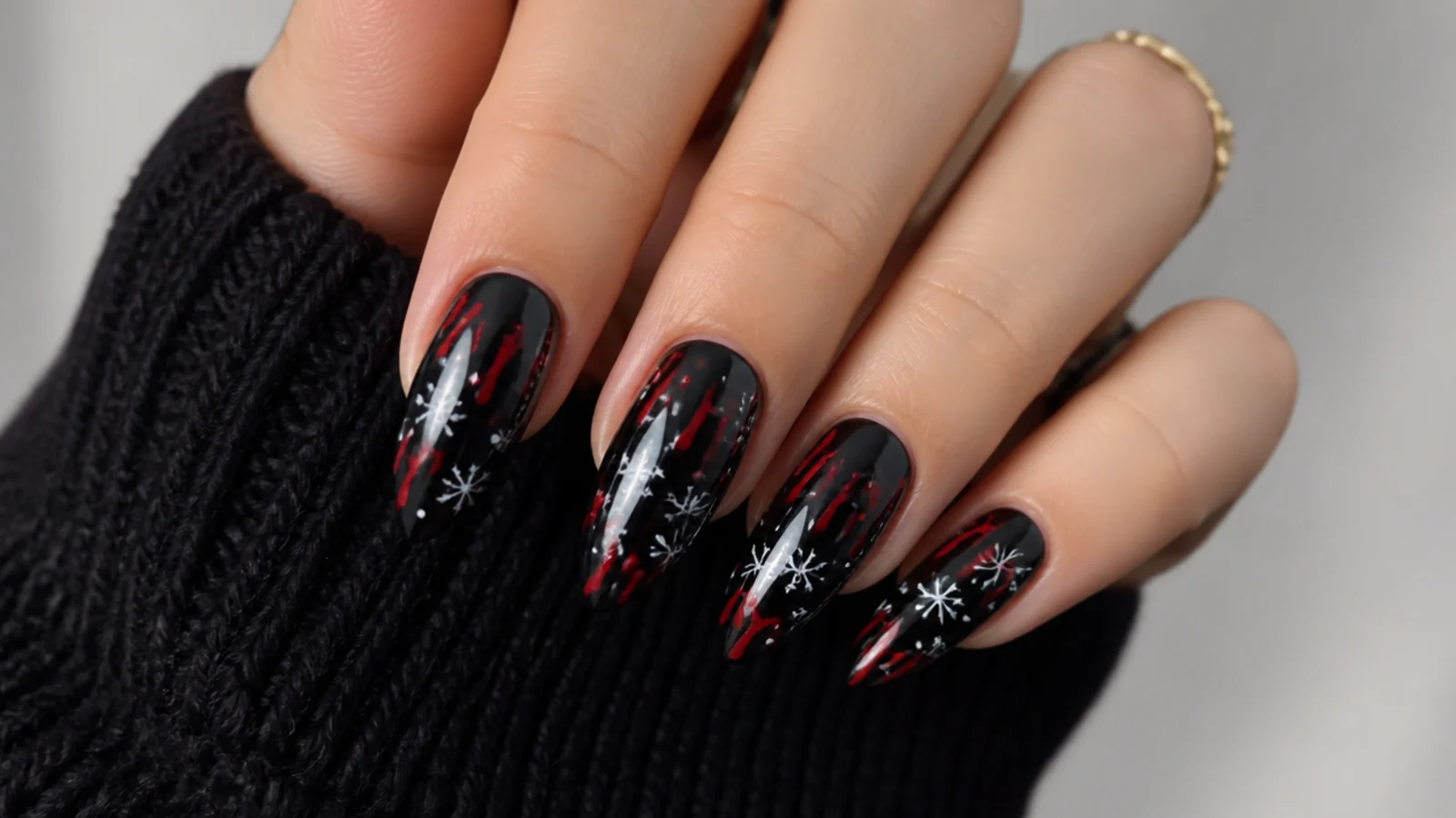 Dark emo Christmas nails with black base, red drips and tiny white snowflakes on almond nails
