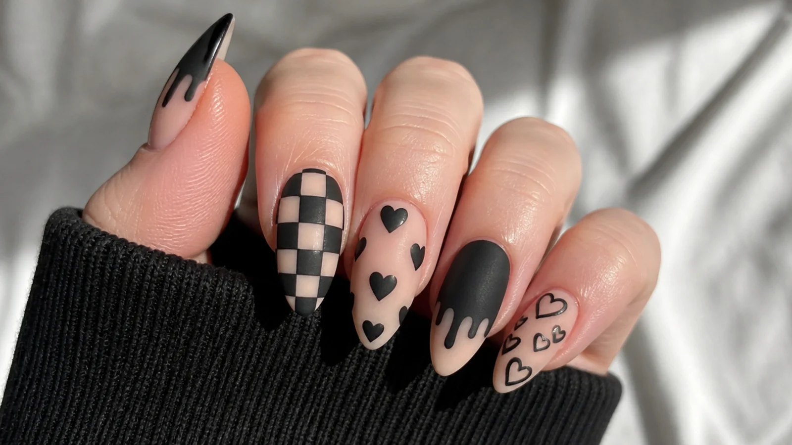Black emo nails with checkerboard, hearts and drip motifs on almond tips