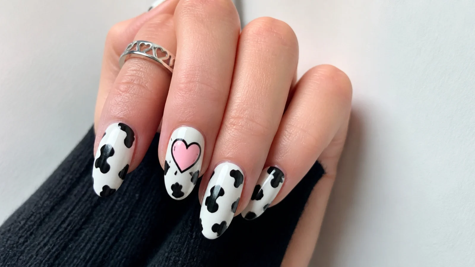 White emo nails with black cow-print patches and a pink heart accent