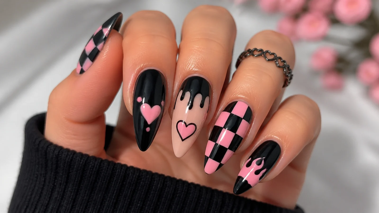 Black and pink emo nails with checkerboard, hearts and dripping motifs on an almond shape