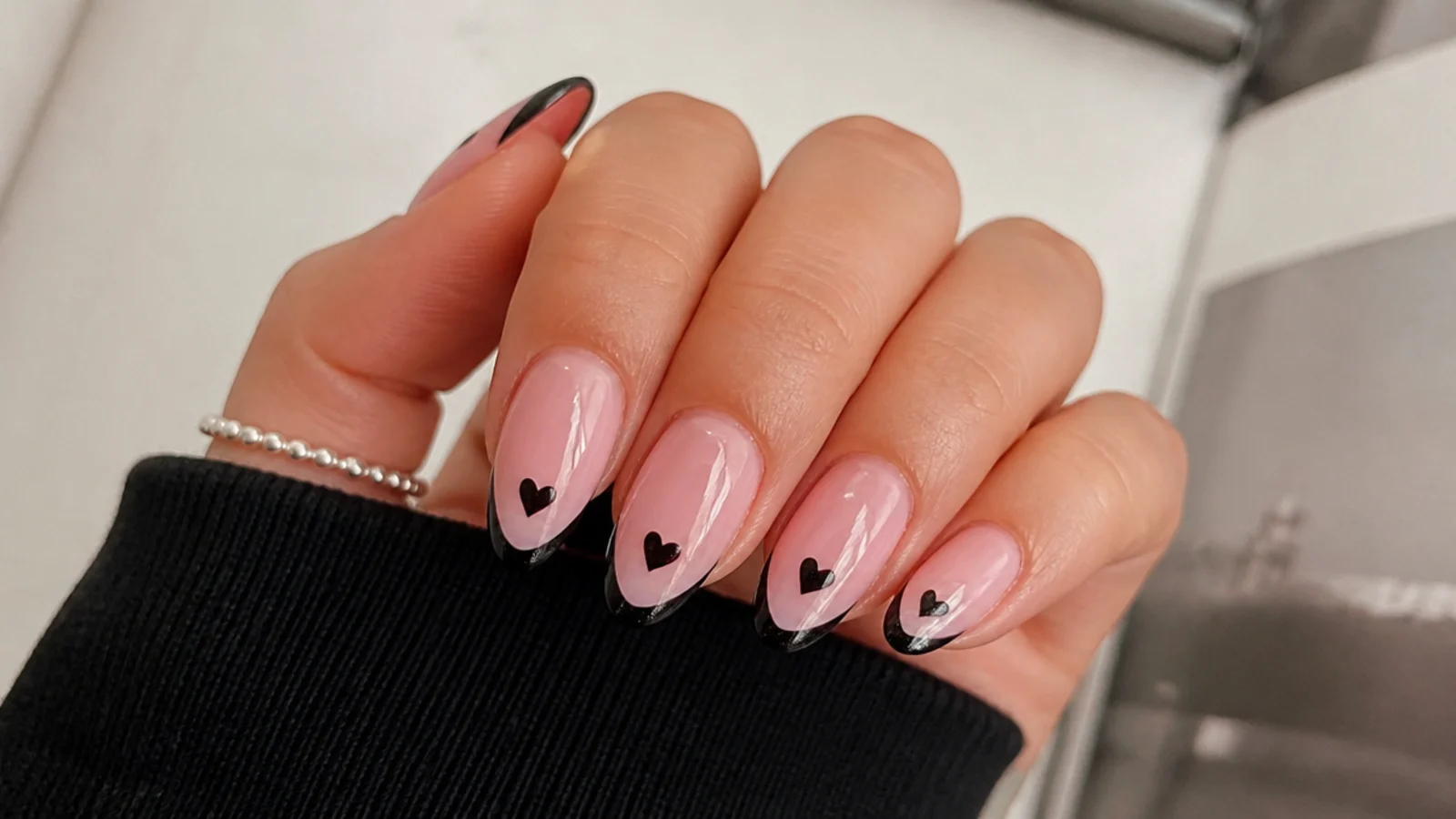 Soft pink emo nails with small black hearts on the tips