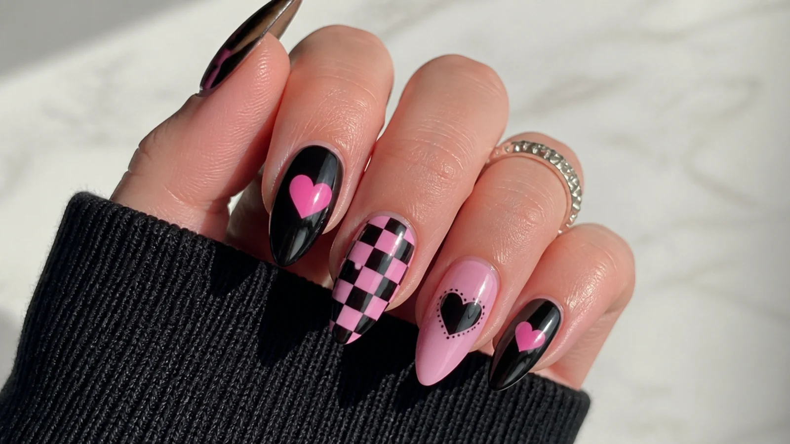 Glossy black emo nails with pink hearts and checkerboard accents on almond tips